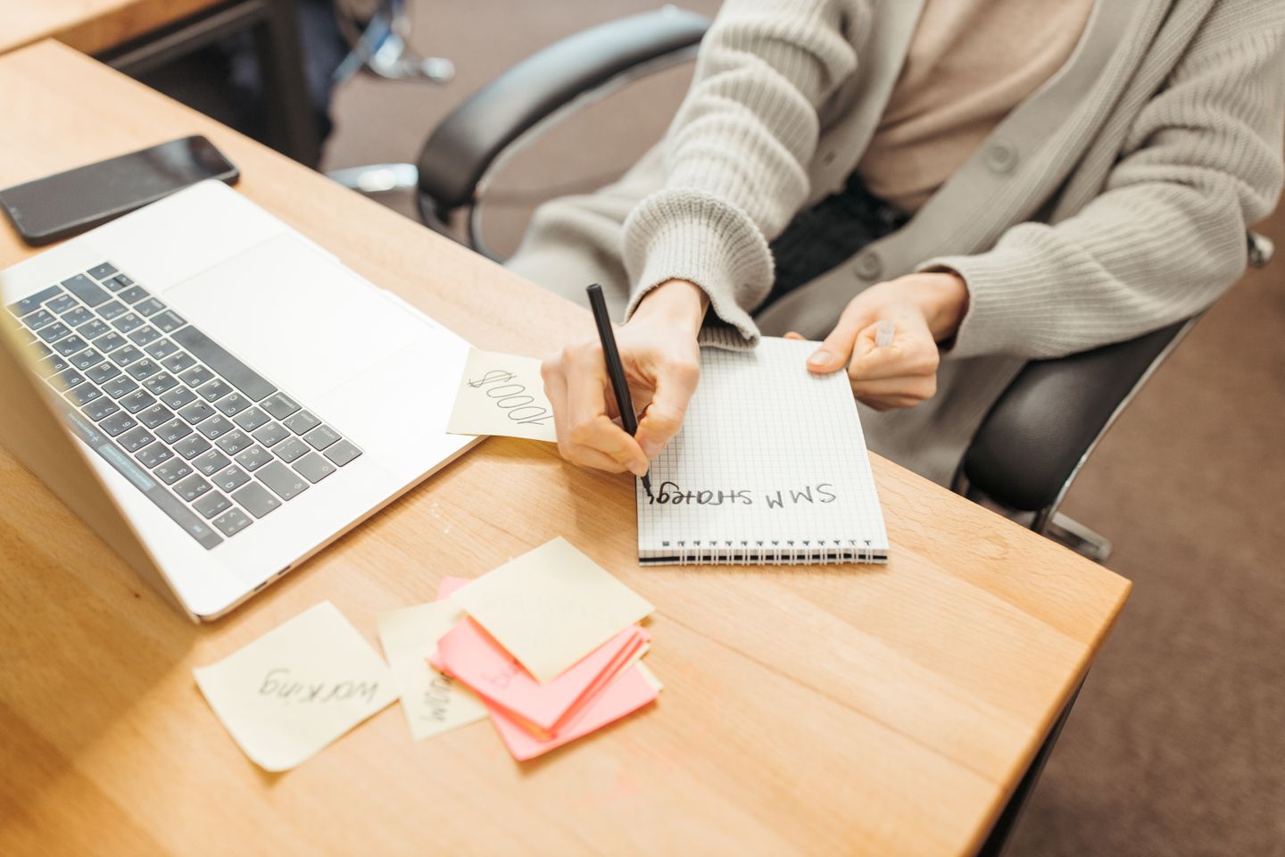 A person planning work in a notebook beside a laptop.