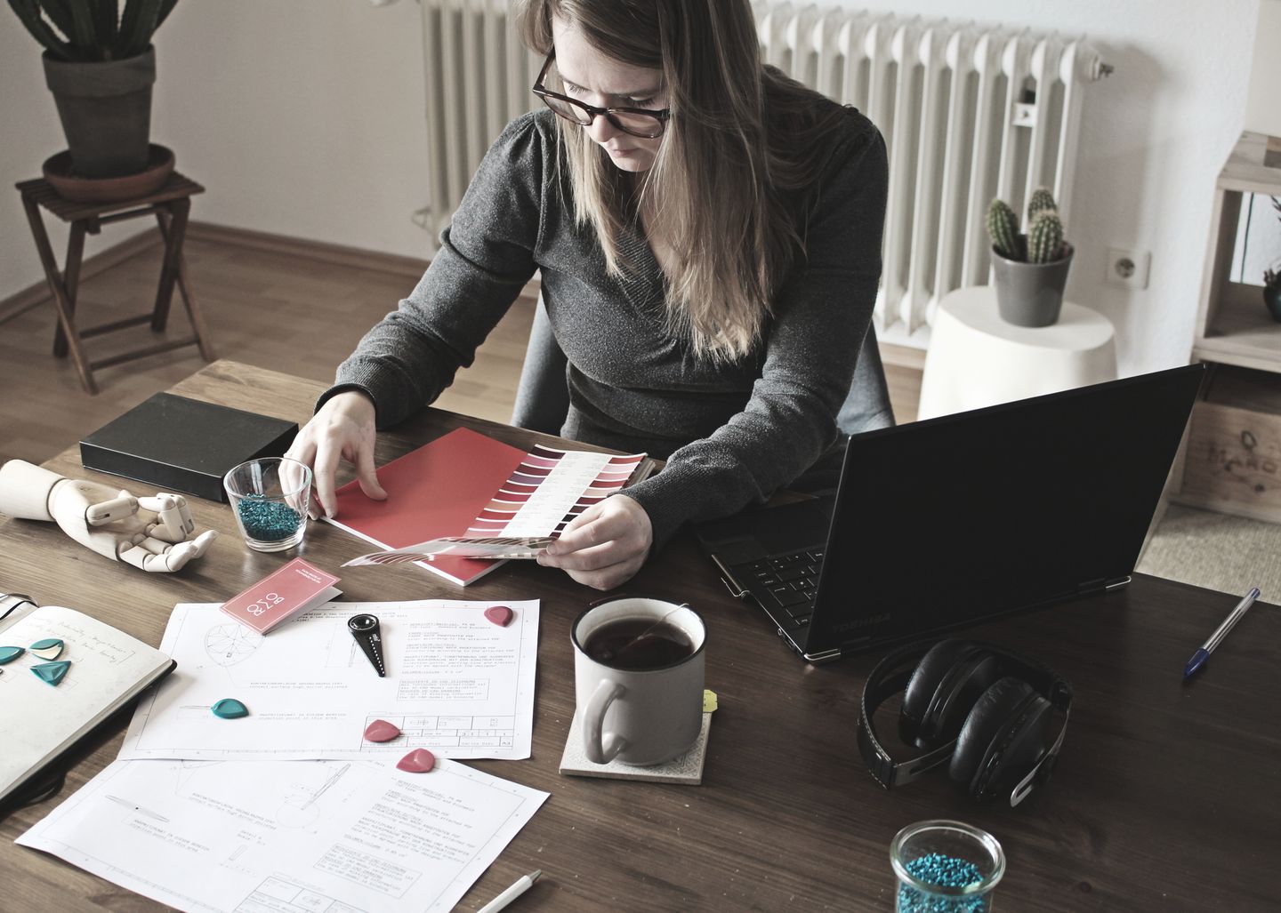 A designer working with a laptop, papers and colour samples.
