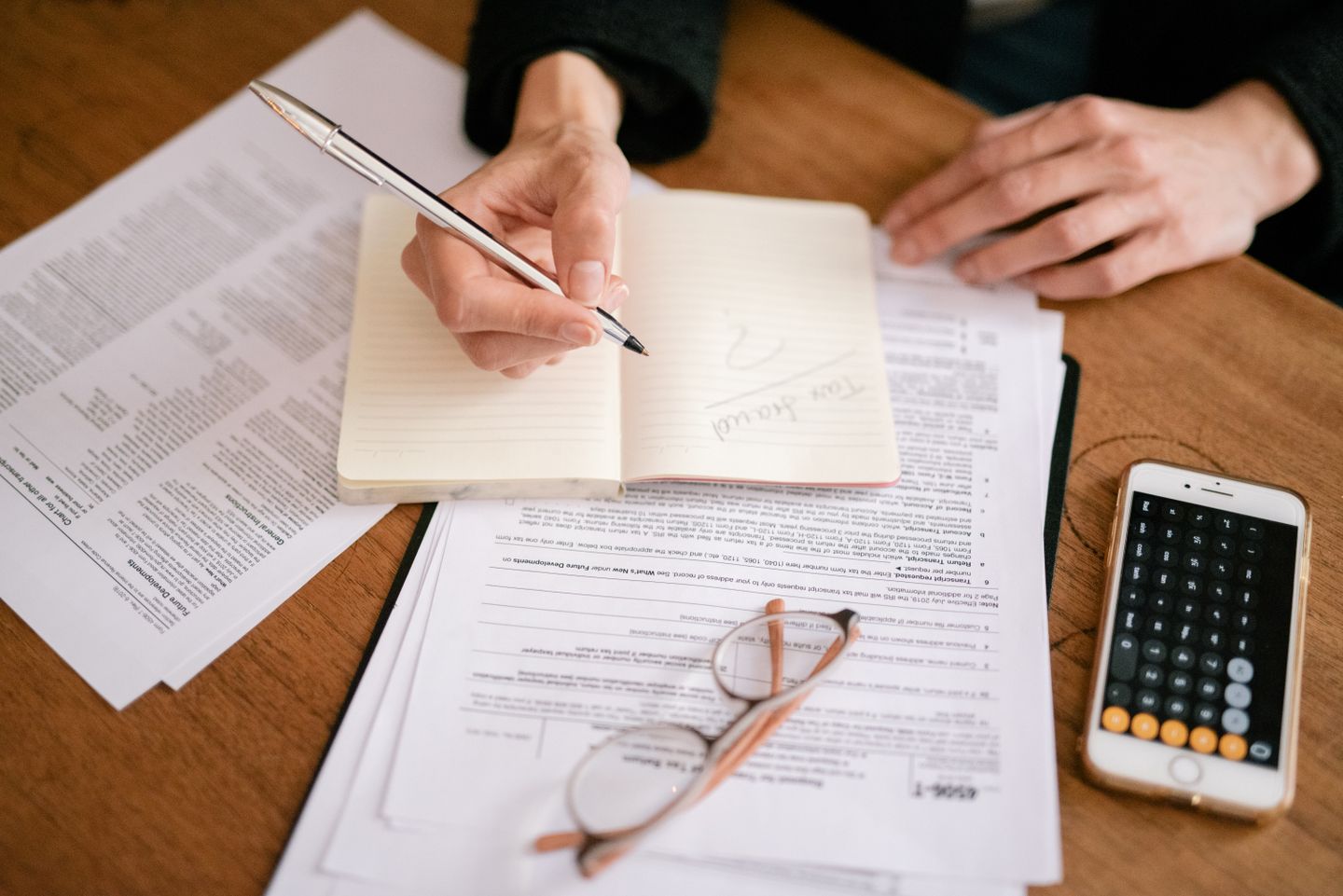 A person reviewing documents and writing beside a calculator.