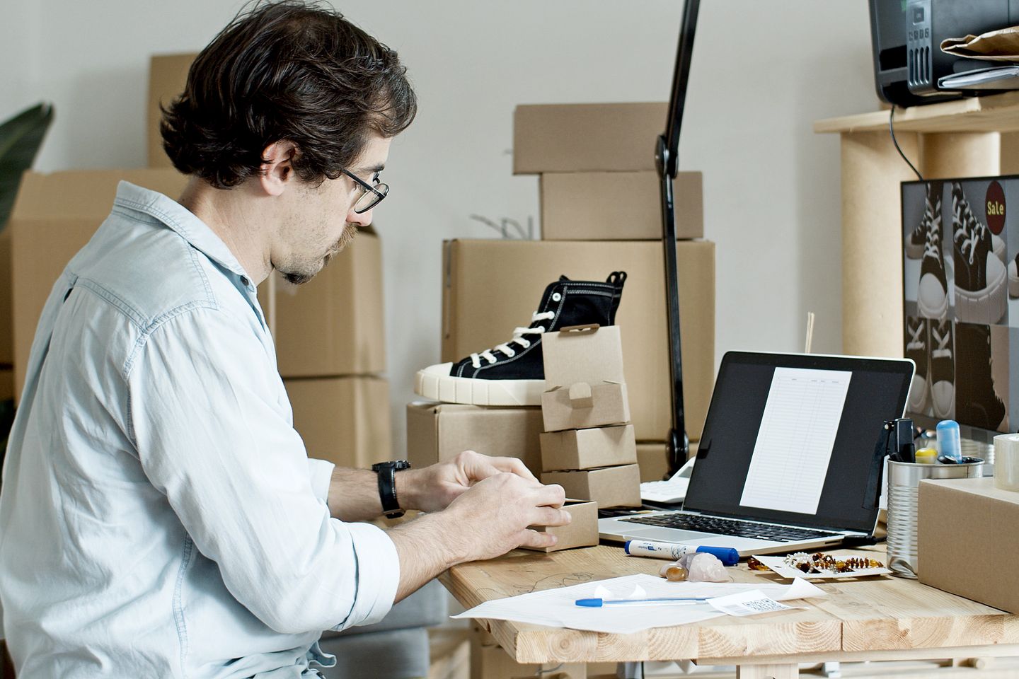 A small-business owner preparing a parcel beside a laptop.