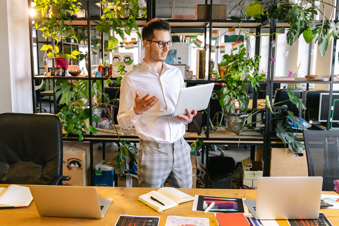 A professional taking a video call at a desk with laptops and plants.